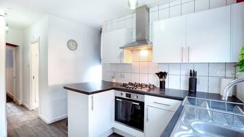 A compact kitchen with white cabinets, a gas stove, an oven, and a stainless steel sink.