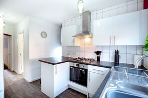 Eine kompakte Küche mit weißen Schränken, einem Gasherd, einem Backofen und einer Edelstahl-Spüle.