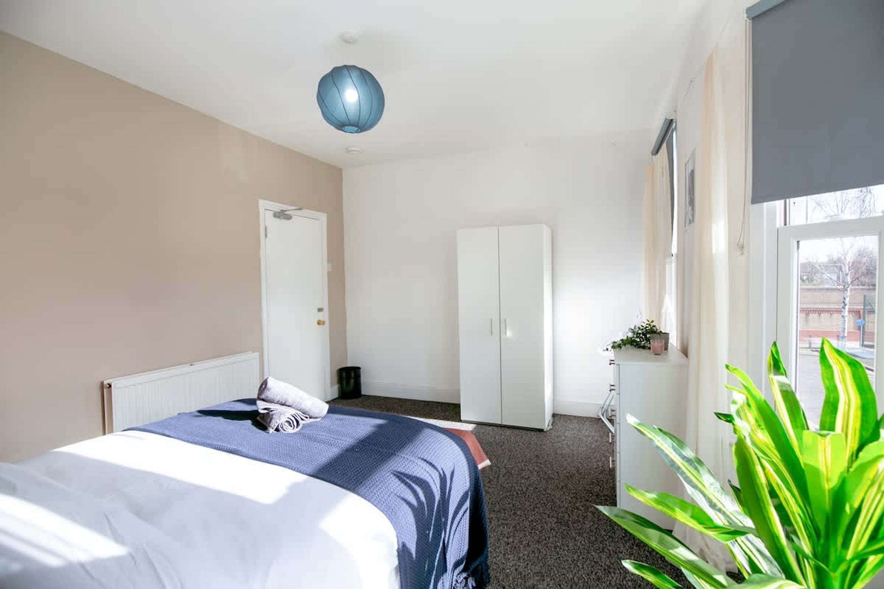 A hotel room with a bed, wardrobe, radiator, and a large window.