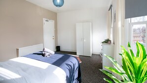 A hotel room with a bed, wardrobe, radiator, and a large window. - Perfect Booking 4 Bed Home in Leytonstone (London)