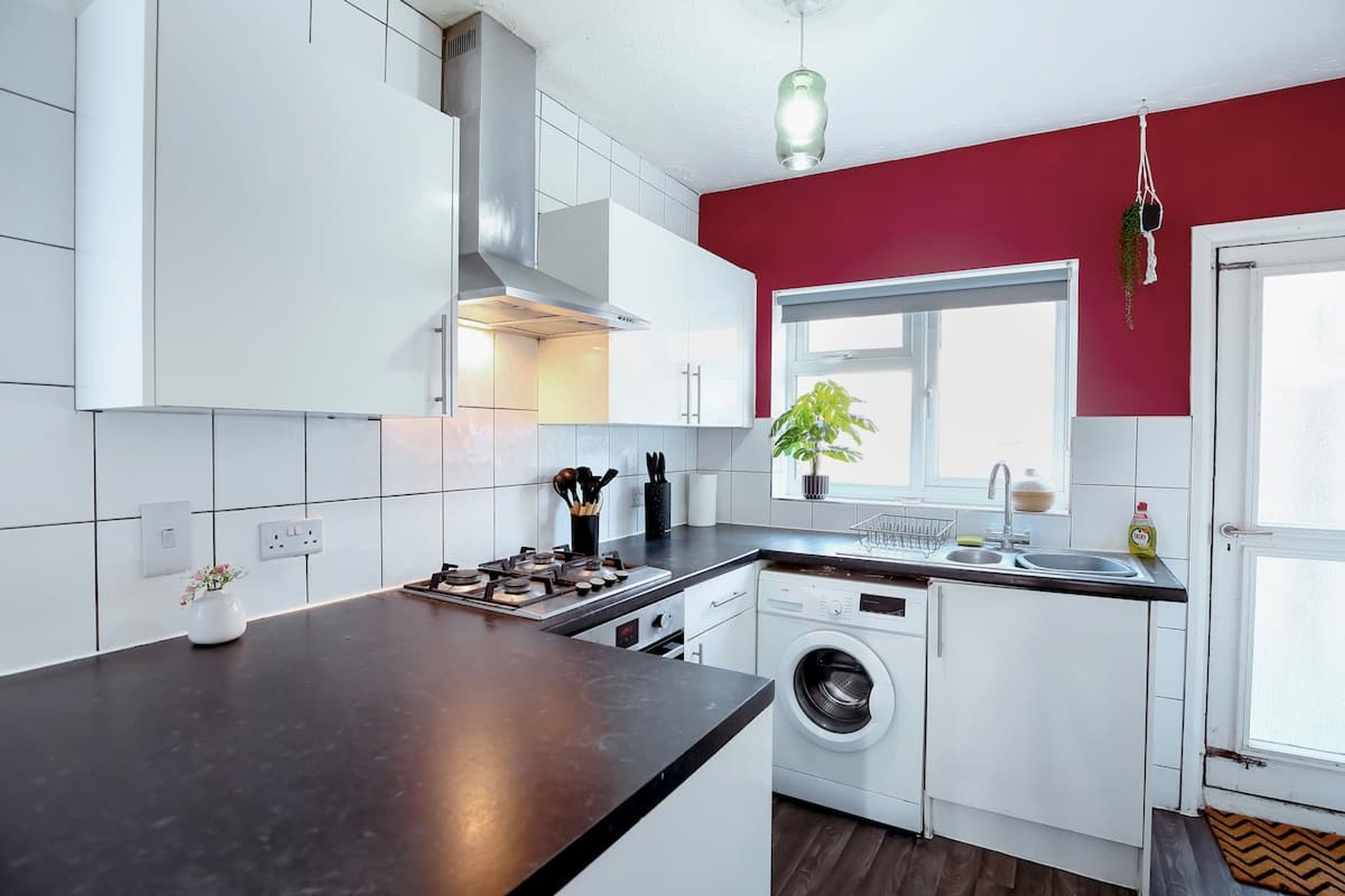 A modern kitchen with white cabinets, a black countertop, a built-in washing machine, and a window with a plant.