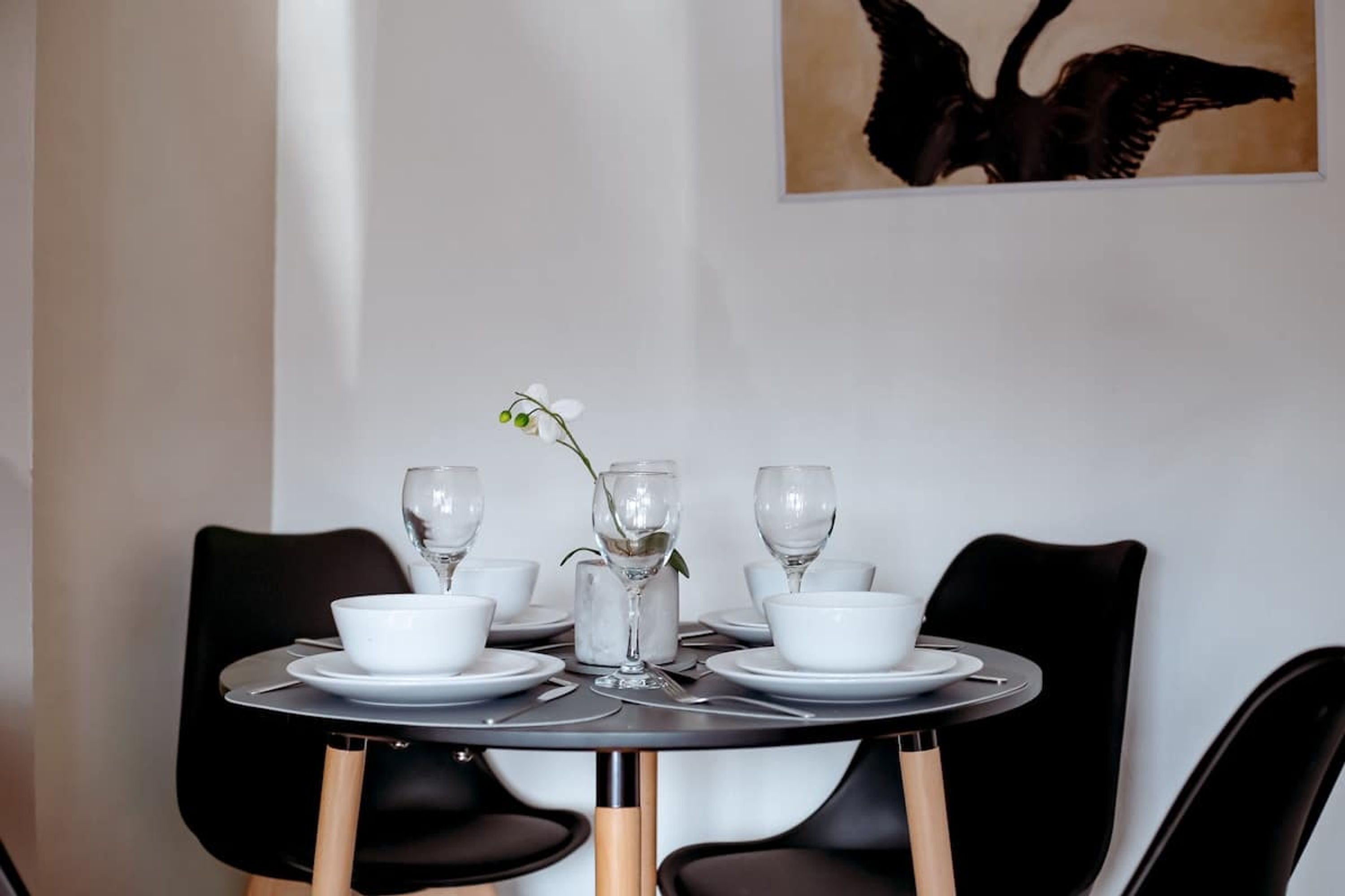 A dining table with white plates, bowls, and glasses, surrounded by black chairs.