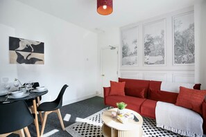 A modern living room with a dining area, a red sofa, and a framed nature scene on the wall. - Perfect Booking 4 Bed Home in Leytonstone (London)