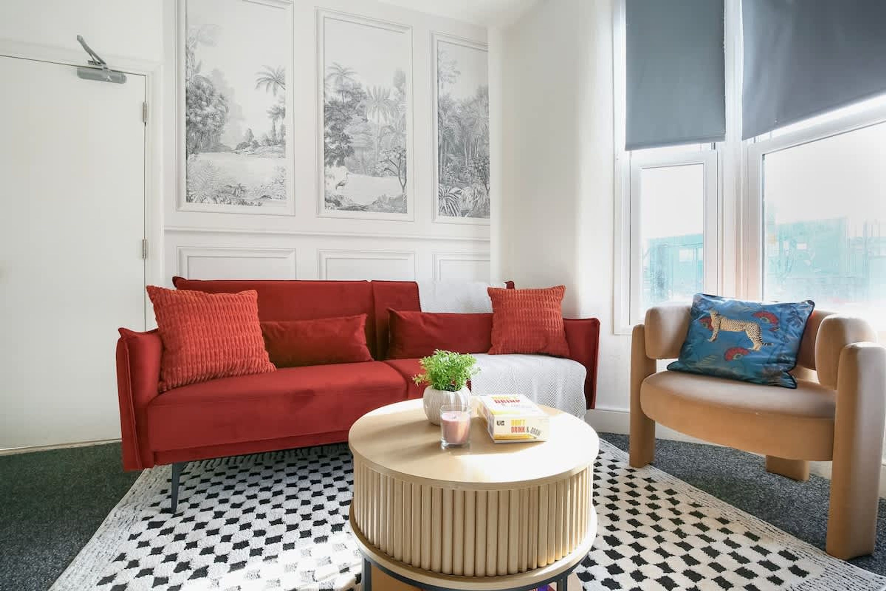A room with a red sofa, a round coffee table with a plant, a blue cushion, and a checkered rug.