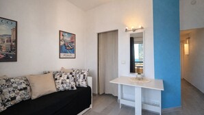 Un salon moderne avec un canapé noir, des coussins à motifs, une console blanche et une affiche encadrée représentant un paysage urbain.