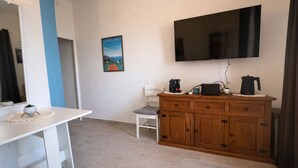Une chambre moderne équipée d’un téléviseur à écran plat, d’une armoire en bois, d’une table blanche et d’une chaise.