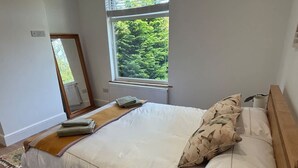 Ein Schlafzimmer mit Bett, einem Fenster mit Blick auf Grünflächen, einem Spiegel und einer Heizung.