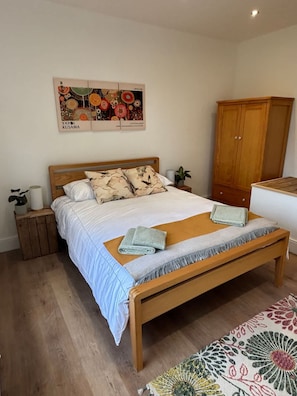Quarto com cama de madeira, mesa de cabeceira, guarda-roupa e uma obra de arte na parede.