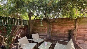 Eine Terrasse mit Metallstühlen und einem Tisch, umgeben von einer Ziegelmauer und Grünpflanzen.