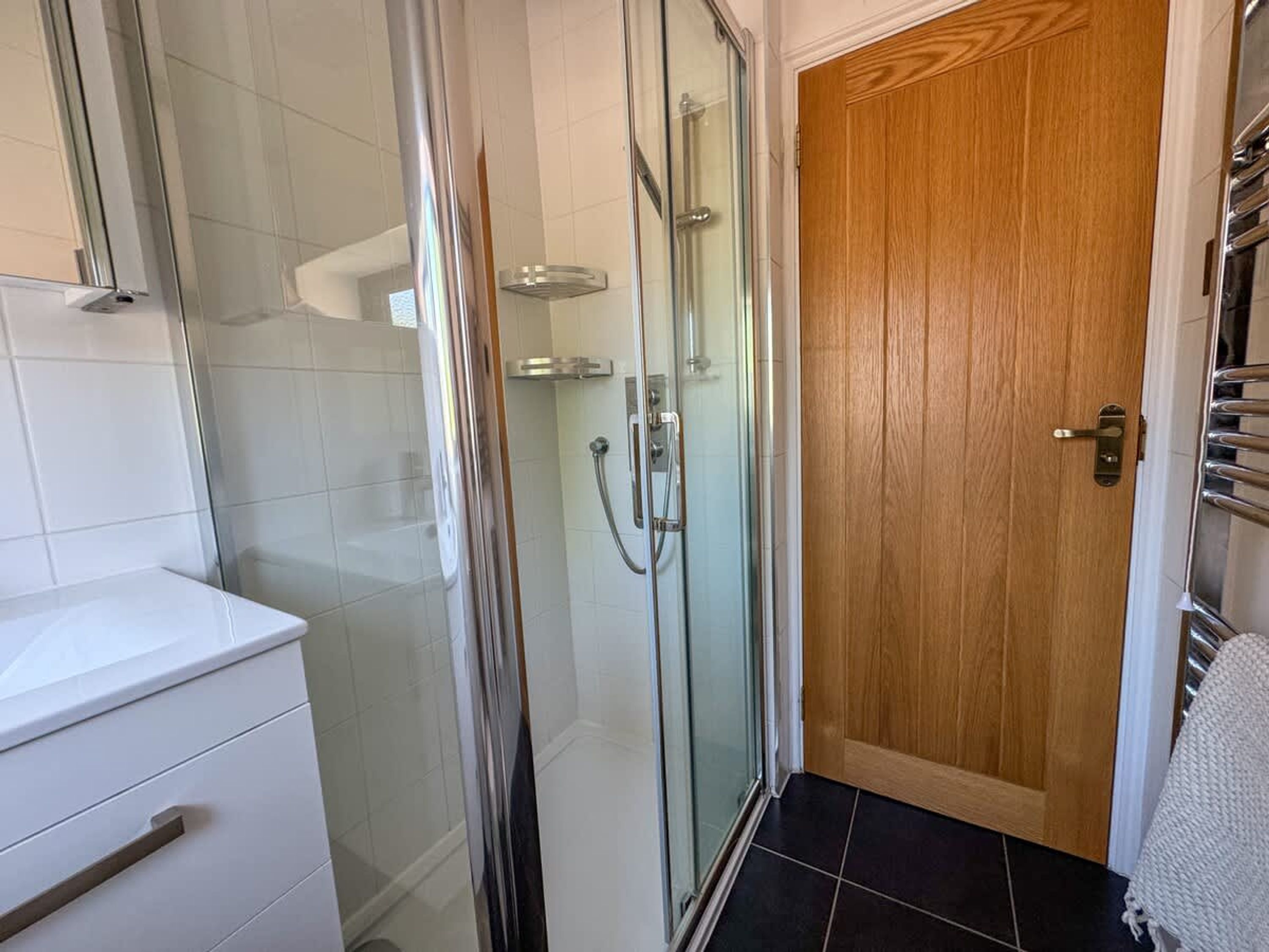 Une salle de bain avec une douche à parois de verre, une porte en bois et un comptoir blanc.
