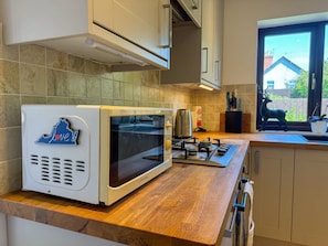 Une cuisine équipée d’un four encastré, d’une cuisinière à gaz et d’une fenêtre donnant sur une maison.