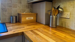 Eine Küche mit Holztischplatte, einer Brokasten, einem Metall-Utensilienhalter und einer gefliesten Spritzschutzwand.