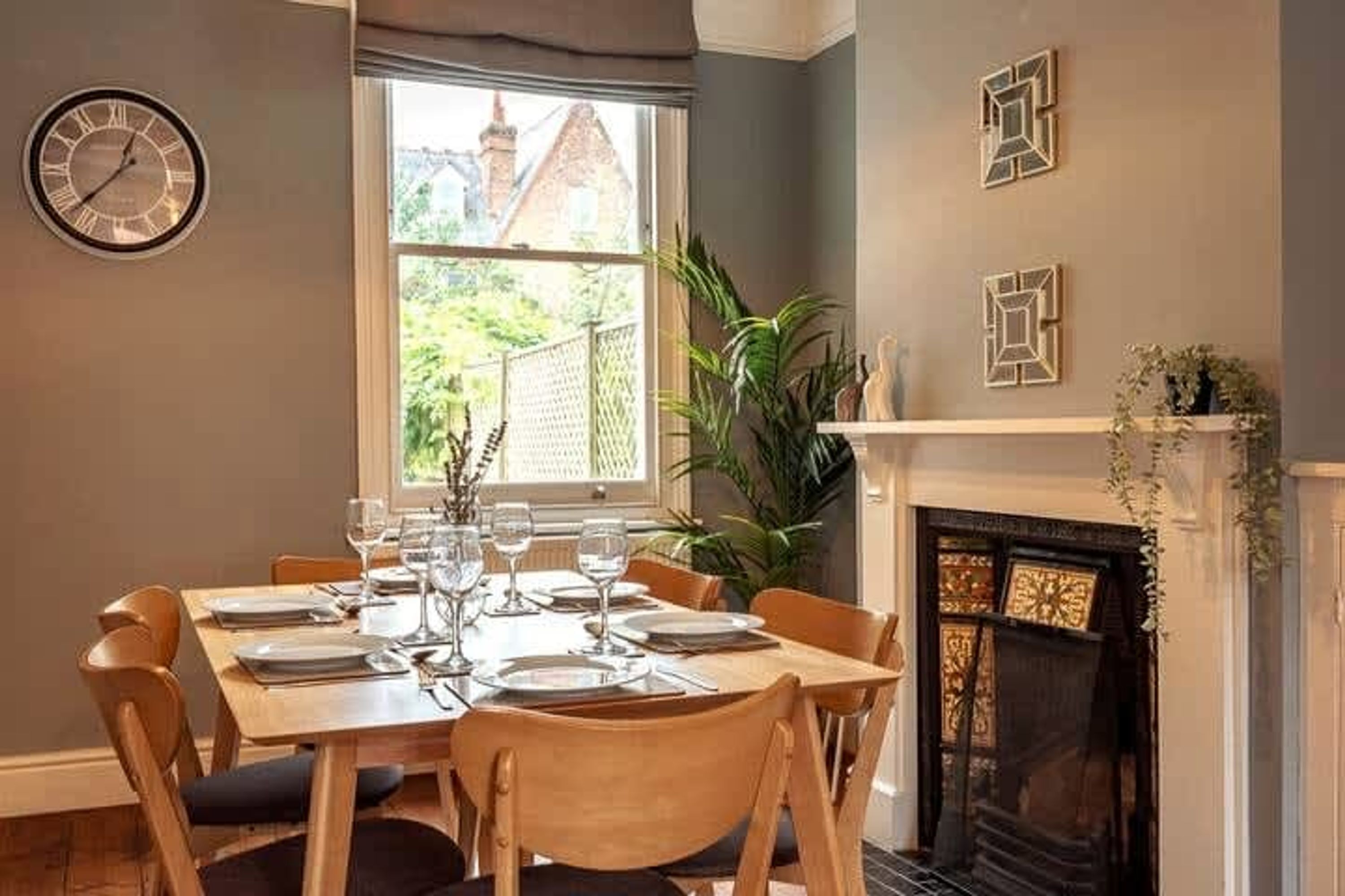 Une salle à manger avec une table dressée pour six personnes, une cheminée et une fenêtre donnant sur un bâtiment en briques.