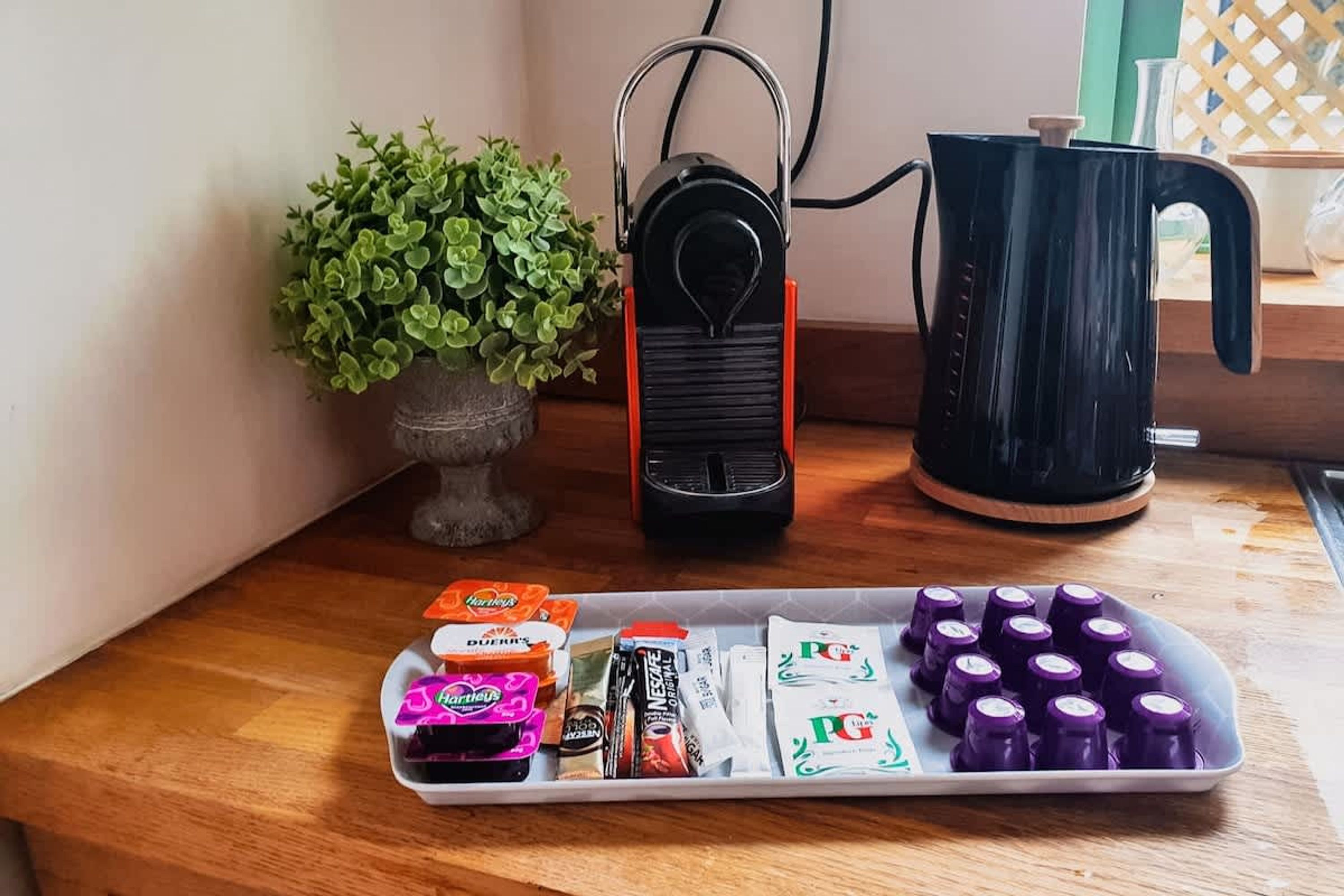 A kitchen counter with a coffee maker, a kettle, and a tray of coffee pods.