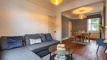 A living room with a sofa, a coffee table with books, a dining area with a table and chairs, and a window with a view.
