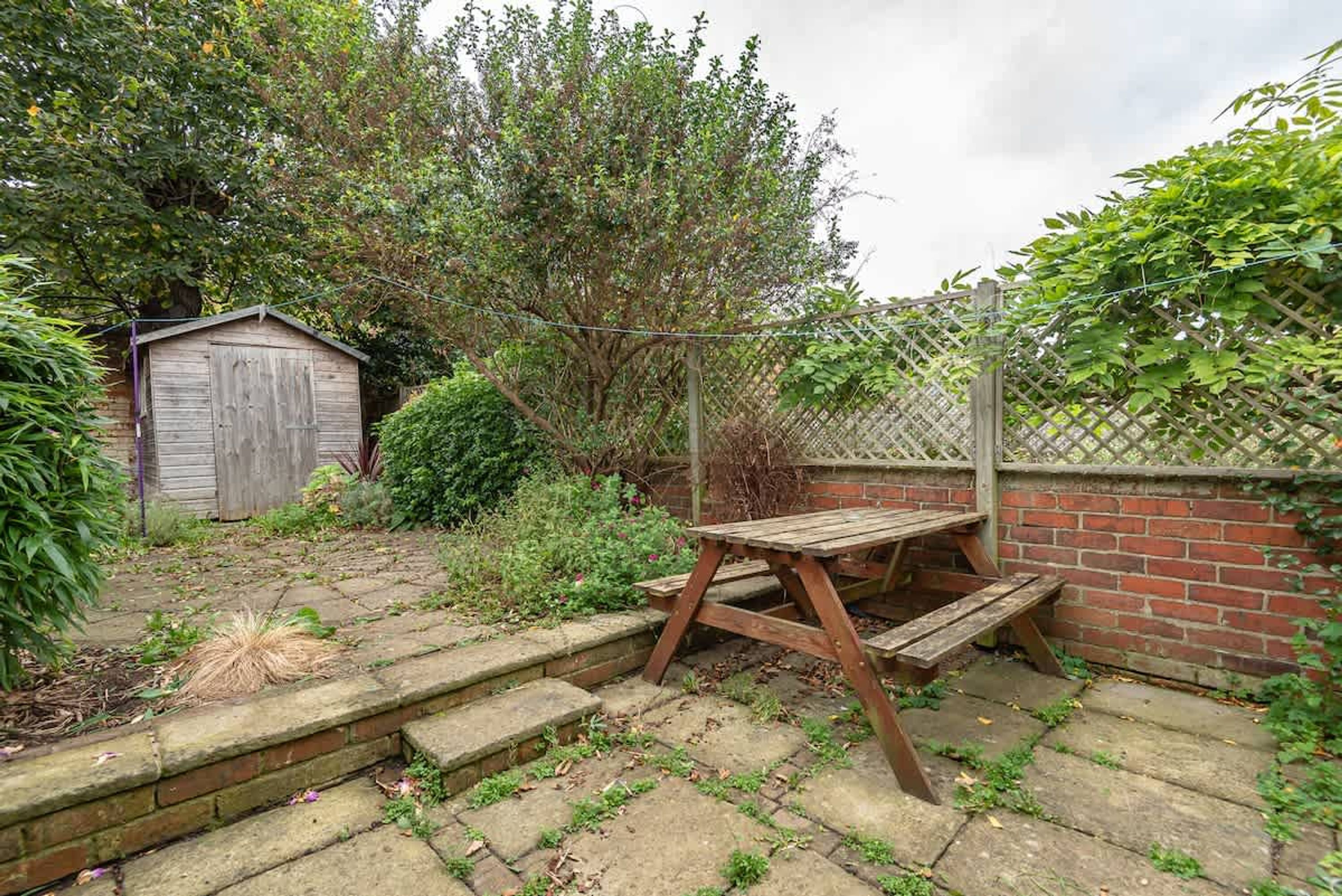 Un jardín con una mesa de madera y escalones que conducen a un cobertizo.