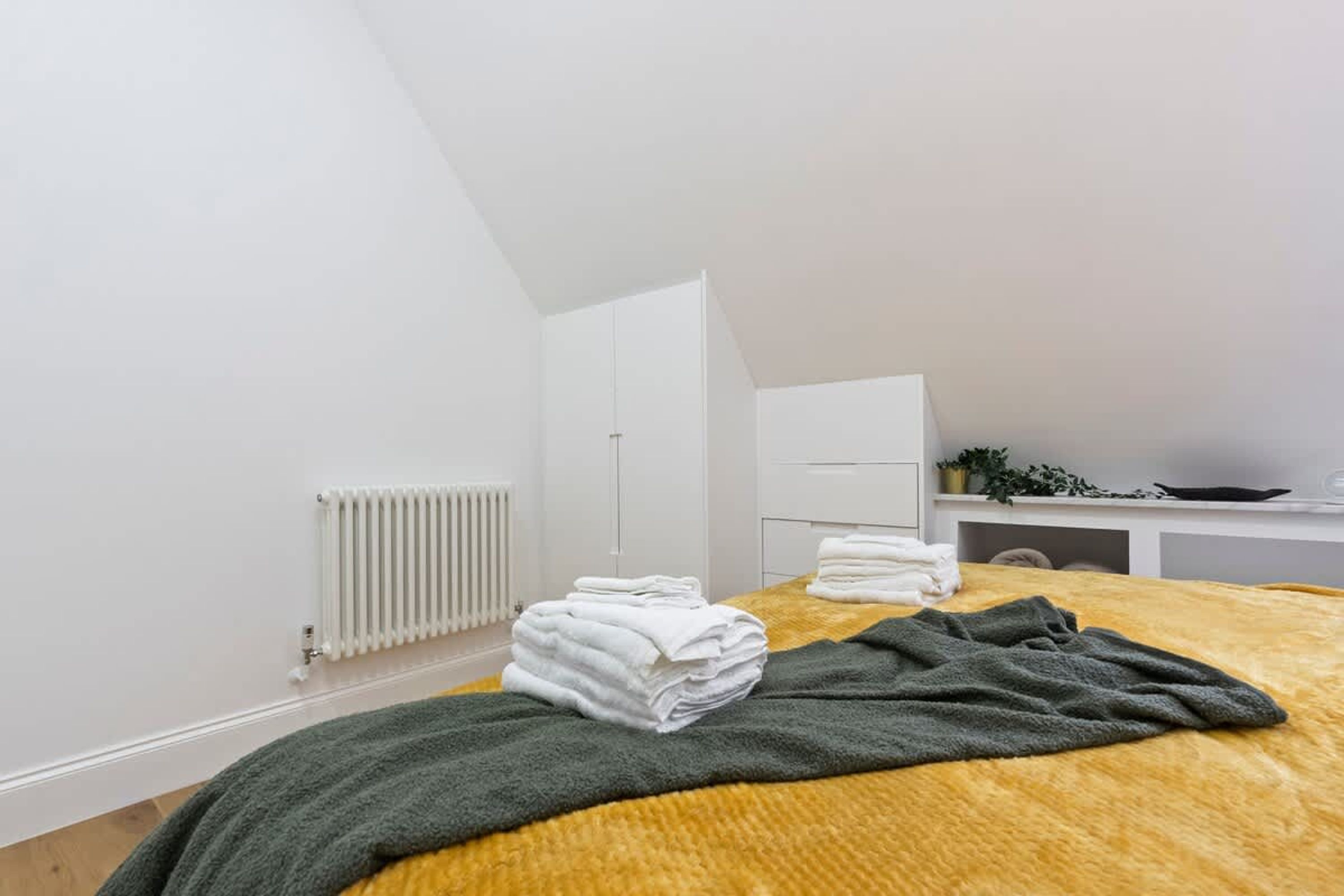 Ein Schlafzimmer mit einem Bett, einem Heizkörper, einem Schreibtisch und einem Regal mit Pflanzen.
