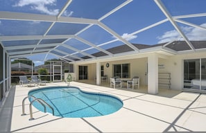 A covered outdoor swimming pool with lounge chairs and a table, surrounded by a white building with large windows. - Villa Grandjean 4 Bedroom With Private Pool (Inverness)