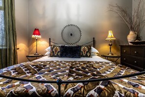 Ein rundes Bett mit gemustertem Überwurf, zwei Nachttischlampen, einer Wanddekoration und einer Vase mit Zweigen.