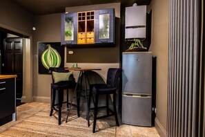 Eine kompakte Küche mit Kühlschrank, eine Essecke mit zwei Stühlen und eine Schrank mit Glastüren.