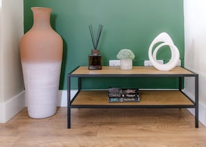Un interior moderno con una pared verde, un jarrón blanco alto, una consola de madera con libros y una escultura abstracta blanca.