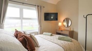 A hotel room with a bed, a TV, a bedside table with a lamp, and a window with curtains.