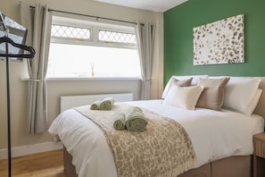 Une chambre à coucher comprenant un lit, un radiateur, une fenêtre avec des rideaux, un tableau décoratif et un porte-serviettes.