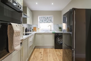 Une cuisine compacte équipée d’un lave-linge, d’un réfrigérateur et d’une fenêtre avec un store à motifs de feuilles.