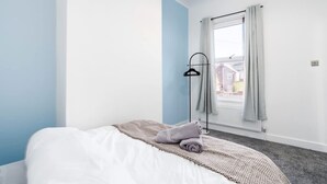 A hotel room with a bed, a window with curtains, a floor lamp, and a view of buildings outside. - Perfect Booking Stylish 3 Bed Family Home (Doncaster)