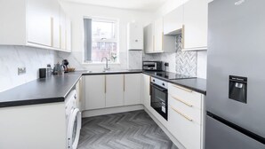 A modern kitchen with white cabinets, a stainless steel refrigerator, and a herringbone-patterned backsplash. - Perfect Booking Stylish 3 Bed Family Home (Doncaster)