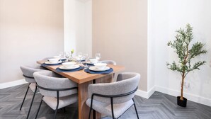 A dining area with a rectangular table set for four, grey upholstered chairs, and a potted plant. - Perfect Booking Stylish 3 Bed Family Home (Doncaster)