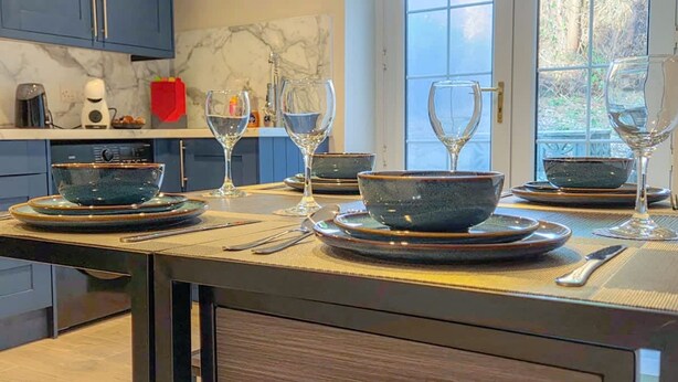 Una cocina con salpicadero de mármol, armarios oscuros y una zona de comedor con cuencos, platos y copas de vino azules.