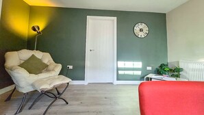 Una habitación con una puerta blanca, un reloj en la pared, una lámpara y una silla.