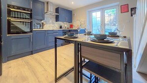 Una cocina moderna con armarios azules, horno empotrado y comedor con una mesa para dos.