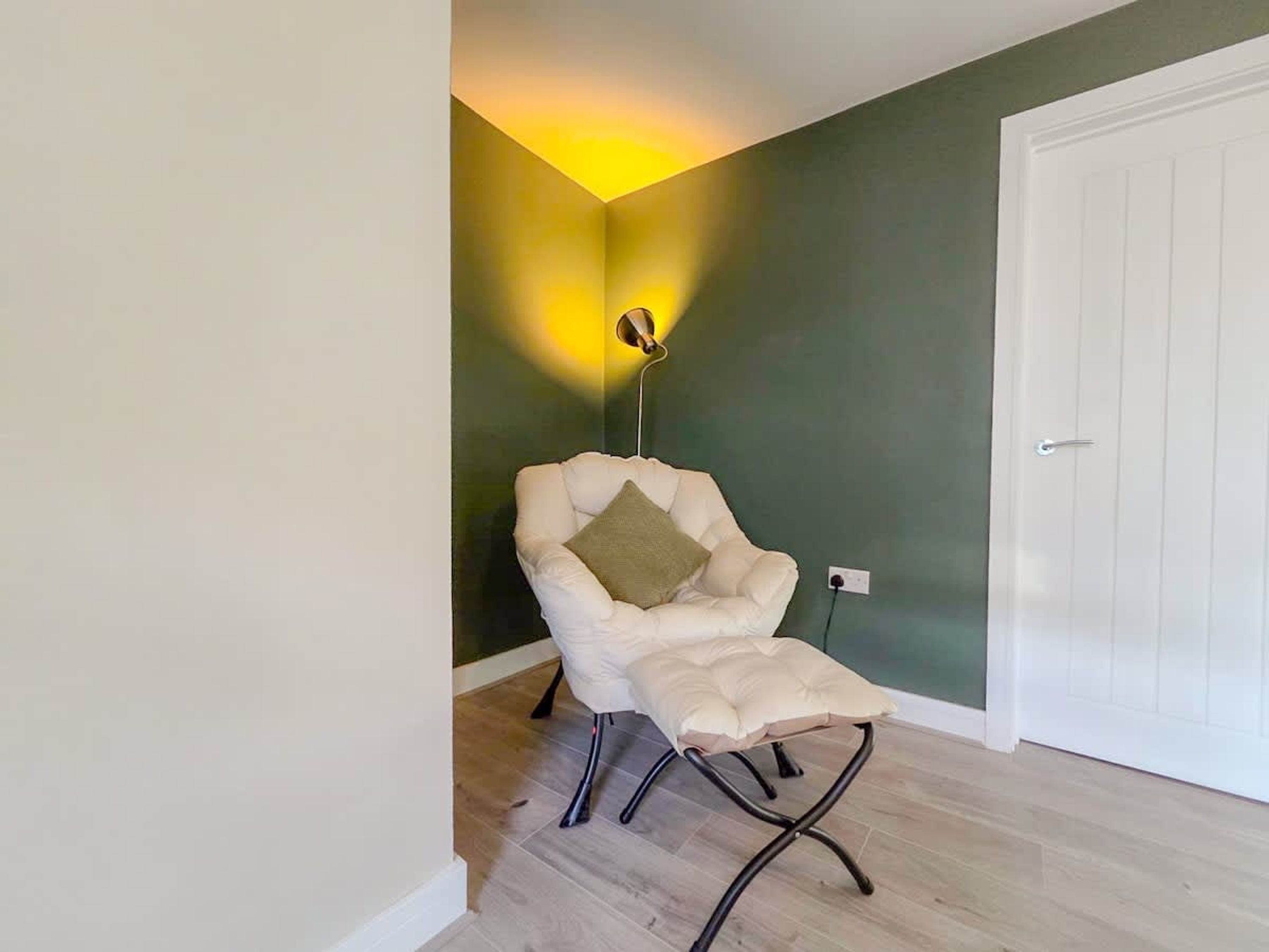 A room with a white chair, a wall-mounted lamp, and a white door.
