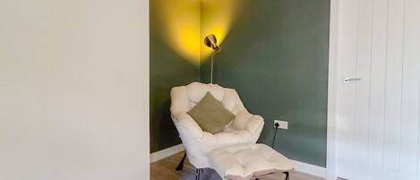 A room with a white chair, a wall-mounted lamp, and a white door.
