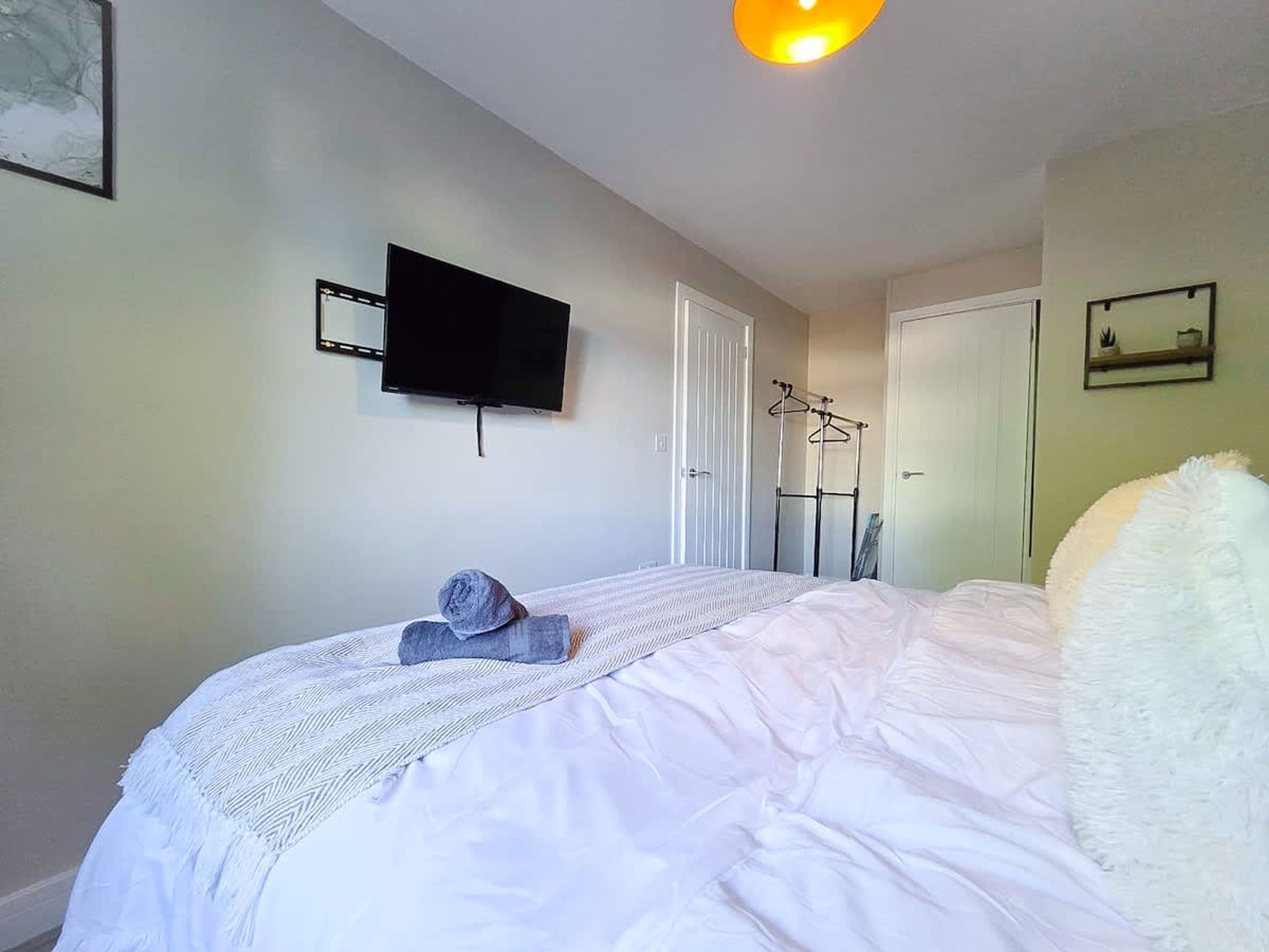Een slaapkamer met een bed, een aan de muur bevestigde televisie, een deur en een kapstok.