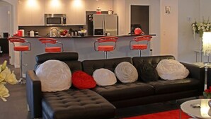 Ein modernes Wohnzimmer mit einer schwarzen Ledersofa, roten und weißen Kissen, einem roten Teppich und einer Küche im Hintergrund.