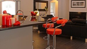 Eine moderne Küche mit Kochinsel, Barhocker, einem schwarzen Sofa und einem Kronleuchter.