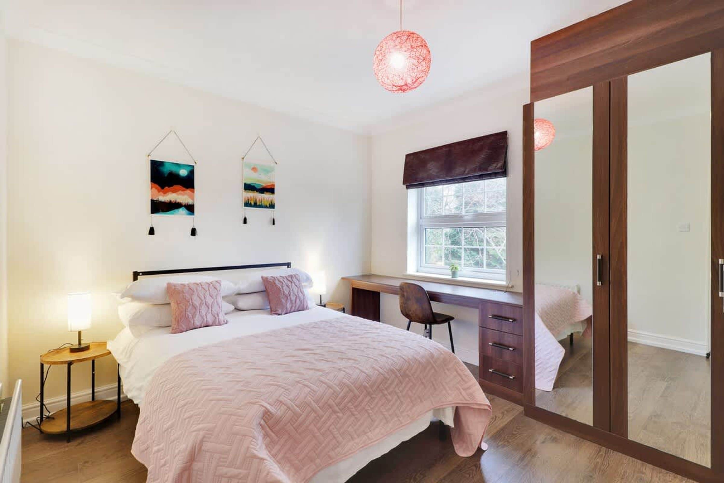 Une chambre à coucher comprenant un lit, une table de chevet, un bureau, une chaise, une fenêtre et une armoire.