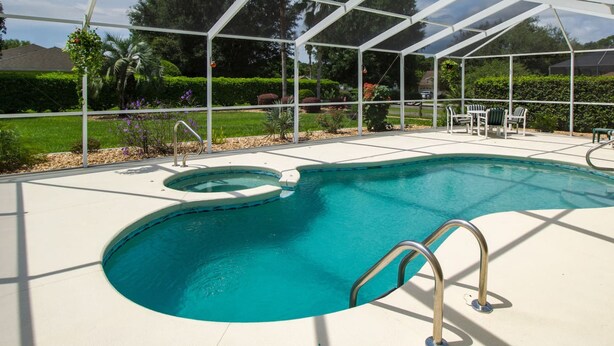 Piscina com vedação de vidro, rodeada por um jardim ajardinado e área de estar coberta.