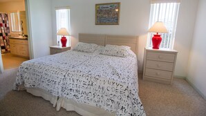 Quarto com cama, duas mesas de cabeceira, um criado-mudo, espelho, janela e um quadro na parede.