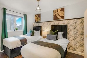 A hotel room with two beds, a window with curtains, a hanging light fixture, and wall art. - Perfect Booking 3 Bed Home in Whitechapel (London)