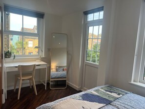Quarto com escrivaninha, cadeira, cama e janelas amplas.