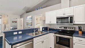 Una cucina moderna con mobili bianchi, un piano di lavoro blu, un forno a microonde, un forno e un lavello.