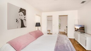 Quarto com cama, televisão, pintura e porta que dá para outro cômodo.