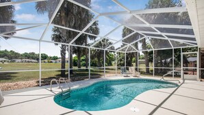 Piscina com cobertura de vidro, rodeada por palmeiras e céu claro.