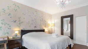 Un dormitorio con una cama grande, dos lámparas de noche, una mesita de noche, un espejo y una pared con estampado floral.