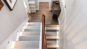 Una escalera con barandilla de madera, escalones alfombrados y una puerta blanca al final.