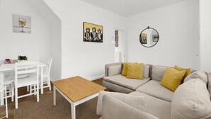 Ein modernes Wohnzimmer mit einer Couch, einem Holztisch, einem Esstisch mit Stühlen und Wandbildern.